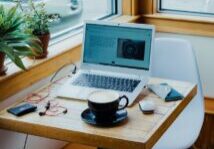 cup of coffee, laptop computer, and red earphones plugged in laptop on brown wooden table